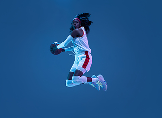 Image showing Beautiful african-american female basketball player in motion and action in neon light on blue background. Concept of healthy lifestyle, professional sport, hobby.