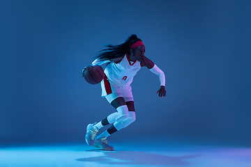 Image showing Beautiful african-american female basketball player in motion and action in neon light on blue background. Concept of healthy lifestyle, professional sport, hobby.