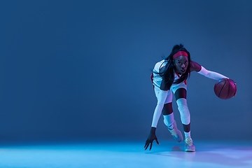 Image showing Beautiful african-american female basketball player in motion and action in neon light on blue background. Concept of healthy lifestyle, professional sport, hobby.