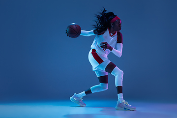 Image showing Beautiful african-american female basketball player in motion and action in neon light on blue background. Concept of healthy lifestyle, professional sport, hobby.