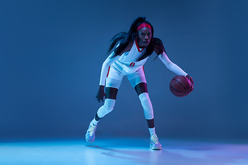 Image showing Beautiful african-american female basketball player in motion and action in neon light on blue background. Concept of healthy lifestyle, professional sport, hobby.