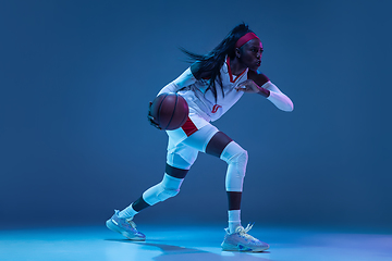 Image showing Beautiful african-american female basketball player in motion and action in neon light on blue background. Concept of healthy lifestyle, professional sport, hobby.