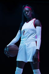 Image showing Beautiful african-american female basketball player in motion and action in neon light on black background. Concept of healthy lifestyle, professional sport, hobby.