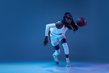 Image showing Beautiful african-american female basketball player in motion and action in neon light on blue background. Concept of healthy lifestyle, professional sport, hobby.