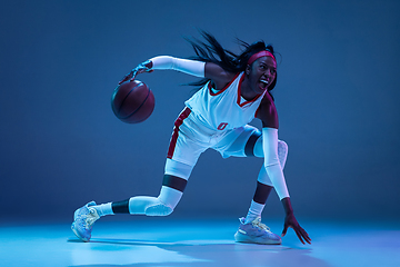 Image showing Beautiful african-american female basketball player in motion and action in neon light on blue background. Concept of healthy lifestyle, professional sport, hobby.