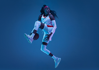 Image showing Beautiful african-american female basketball player in motion and action in neon light on blue background. Concept of healthy lifestyle, professional sport, hobby.