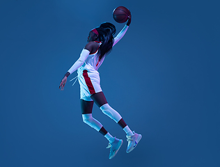 Image showing Beautiful african-american female basketball player in motion and action in neon light on blue background. Concept of healthy lifestyle, professional sport, hobby.