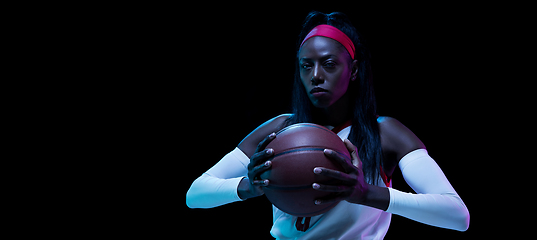 Image showing Beautiful african-american female basketball player in motion and action in neon light on black background. Concept of healthy lifestyle, professional sport, hobby.