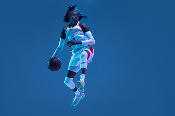 Image showing Beautiful african-american female basketball player in motion and action in neon light on blue background. Concept of healthy lifestyle, professional sport, hobby.