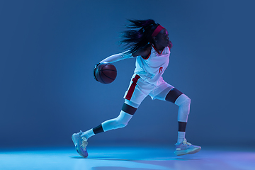 Image showing Beautiful african-american female basketball player in motion and action in neon light on blue background. Concept of healthy lifestyle, professional sport, hobby.