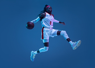 Image showing Beautiful african-american female basketball player in motion and action in neon light on blue background. Concept of healthy lifestyle, professional sport, hobby.