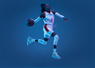 Image showing Beautiful african-american female basketball player in motion and action in neon light on blue background. Concept of healthy lifestyle, professional sport, hobby.