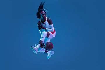 Image showing Beautiful african-american female basketball player in motion and action in neon light on blue background. Concept of healthy lifestyle, professional sport, hobby.