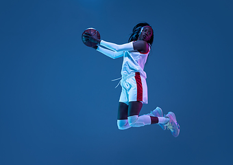 Image showing Beautiful african-american female basketball player in motion and action in neon light on blue background. Concept of healthy lifestyle, professional sport, hobby.