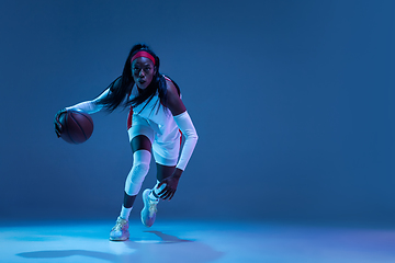 Image showing Beautiful african-american female basketball player in motion and action in neon light on blue background. Concept of healthy lifestyle, professional sport, hobby.