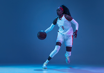 Image showing Beautiful african-american female basketball player in motion and action in neon light on blue background. Concept of healthy lifestyle, professional sport, hobby.