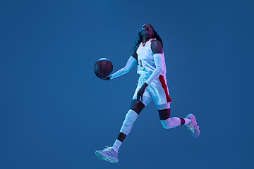 Image showing Beautiful african-american female basketball player in motion and action in neon light on blue background. Concept of healthy lifestyle, professional sport, hobby.