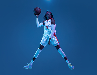 Image showing Beautiful african-american female basketball player in motion and action in neon light on blue background. Concept of healthy lifestyle, professional sport, hobby.