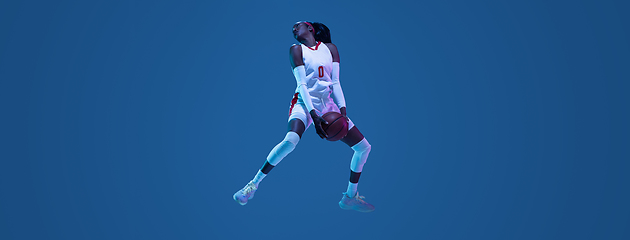 Image showing Beautiful african-american female basketball player in motion and action in neon light on blue background. Concept of healthy lifestyle, professional sport, hobby.