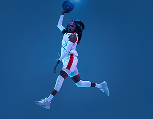 Image showing Beautiful african-american female basketball player in motion and action in neon light on blue background. Concept of healthy lifestyle, professional sport, hobby.