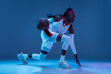 Image showing Beautiful african-american female basketball player in motion and action in neon light on blue background. Concept of healthy lifestyle, professional sport, hobby.