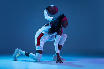 Image showing Beautiful african-american female basketball player in motion and action in neon light on blue background. Concept of healthy lifestyle, professional sport, hobby.