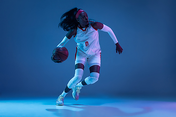 Image showing Beautiful african-american female basketball player in motion and action in neon light on blue background. Concept of healthy lifestyle, professional sport, hobby.