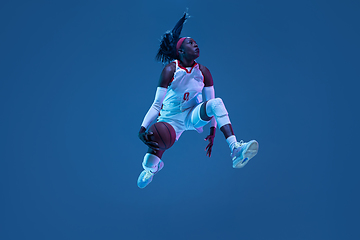 Image showing Beautiful african-american female basketball player in motion and action in neon light on blue background. Concept of healthy lifestyle, professional sport, hobby.