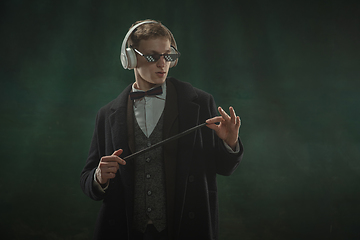 Image showing Young man in art action isolated on dark green background. Retro style, comparison of eras concept.