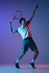 Image showing Young caucasian man playing tennis isolated on purple-blue studio background in neon, action and motion concept