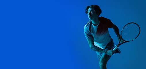 Image showing Young caucasian man playing tennis isolated on blue studio background in neon, action and motion concept