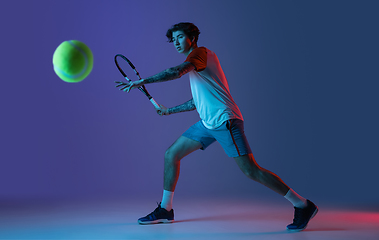 Image showing Young caucasian man playing tennis isolated on purple-blue studio background in neon, action and motion concept