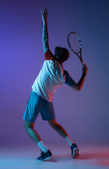 Image showing Young caucasian man playing tennis isolated on purple-blue studio background in neon, action and motion concept