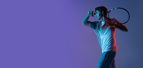 Image showing Young caucasian man playing tennis isolated on purple-blue studio background in neon, action and motion concept