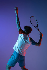 Image showing Young caucasian man playing tennis isolated on purple-blue studio background in neon, action and motion concept