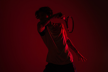 Image showing Young caucasian man playing tennis isolated on red studio background in neon, action and motion concept