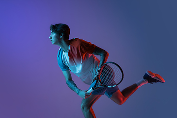 Image showing Young caucasian man playing tennis isolated on purple-blue studio background in neon, action and motion concept