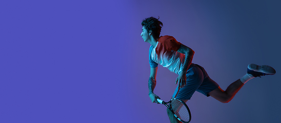 Image showing Young caucasian man playing tennis isolated on purple-blue studio background in neon, action and motion concept