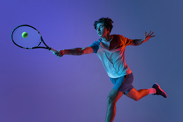 Image showing Young caucasian man playing tennis isolated on purple-blue studio background in neon, action and motion concept