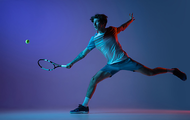 Image showing Young caucasian man playing tennis isolated on purple-blue studio background in neon, action and motion concept