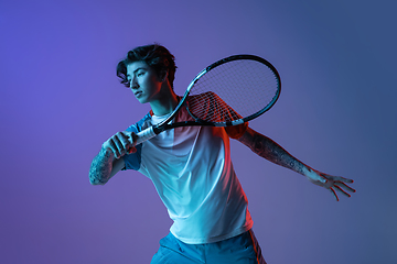 Image showing Young caucasian man playing tennis isolated on purple-blue studio background in neon, action and motion concept