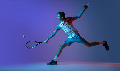 Image showing Young caucasian man playing tennis isolated on purple-blue studio background in neon, action and motion concept