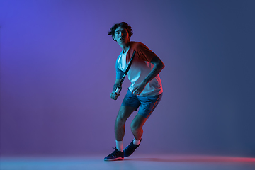 Image showing Young caucasian man playing tennis isolated on purple-blue studio background in neon, action and motion concept