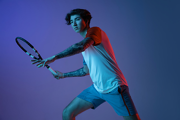 Image showing Young caucasian man playing tennis isolated on purple-blue studio background in neon, action and motion concept