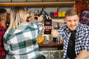 Image showing Man showing phone with betting app on screen. Emotional fans cheering for favourite team, watching on exciting game. Concept of friendship, leisure activity, emotions