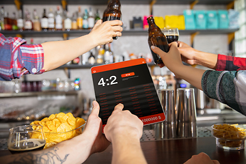 Image showing Man showing phone with betting app on screen. Emotional fans cheering for favourite team, watching on exciting game. Concept of friendship, leisure activity, emotions