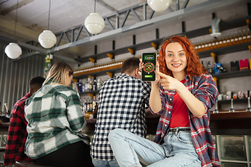 Image showing Woman showing phone with betting app on screen. Emotional fans cheering for favourite team, watching on exciting game. Concept of friendship, leisure activity, emotions