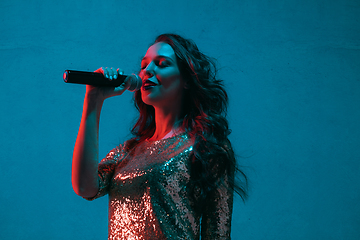 Image showing Caucasian female singer portrait isolated on blue studio background in neon light