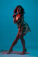 Image showing Caucasian female singer portrait isolated on blue studio background in neon light