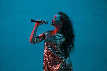 Image showing Caucasian female singer portrait isolated on blue studio background in neon light